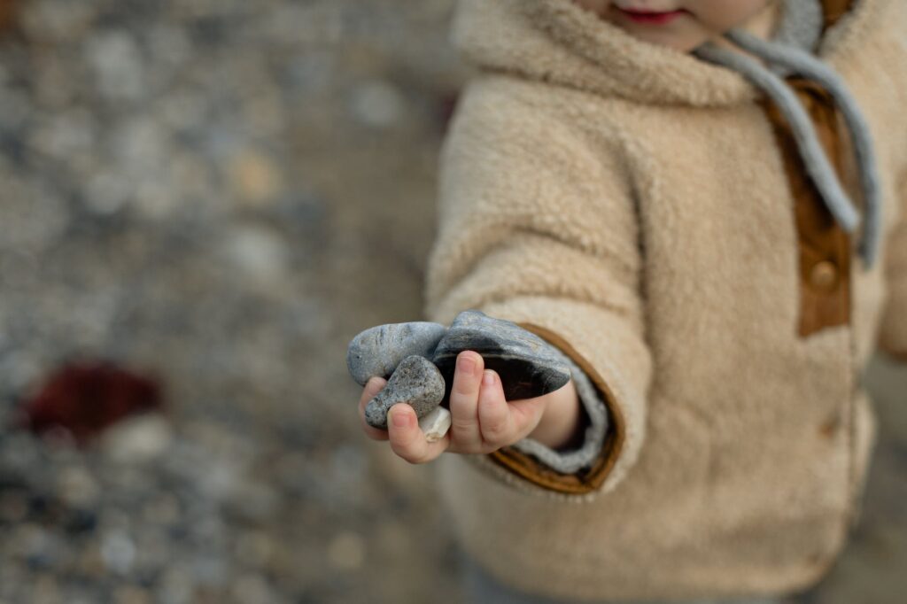 curious little kid in warm coat holding stones in hand on shore